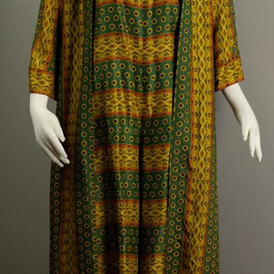 May include: A long green and gold patterned dress with a matching long-sleeved jacket. The dress and jacket have a floral pattern with gold and red accents.