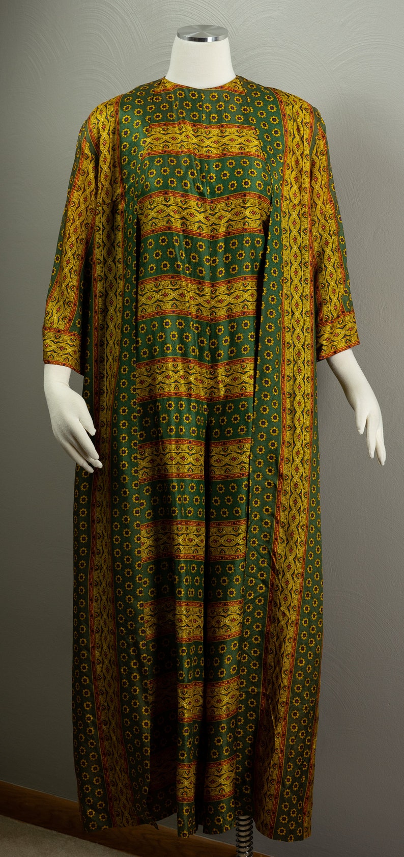 May include: A long green and gold patterned dress with a matching long-sleeved jacket. The dress and jacket have a floral pattern with gold and red accents.