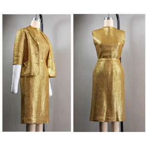 May include: A gold metallic dress and matching jacket set. The dress and jacket have a subtle ribbed texture. The dress is sleeveless and has a fitted silhouette. The jacket has a short sleeve and a single button closure.