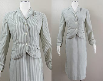 Puede incluir: Un traje vintage de dos piezas con chaqueta y falda. El traje presenta una tela de seersucker con rayas verticales en tonos verdes y blancos. La chaqueta tiene cuello con solapas, cierre de botones y dos bolsillos delanteros. La falda es de estilo lápiz.