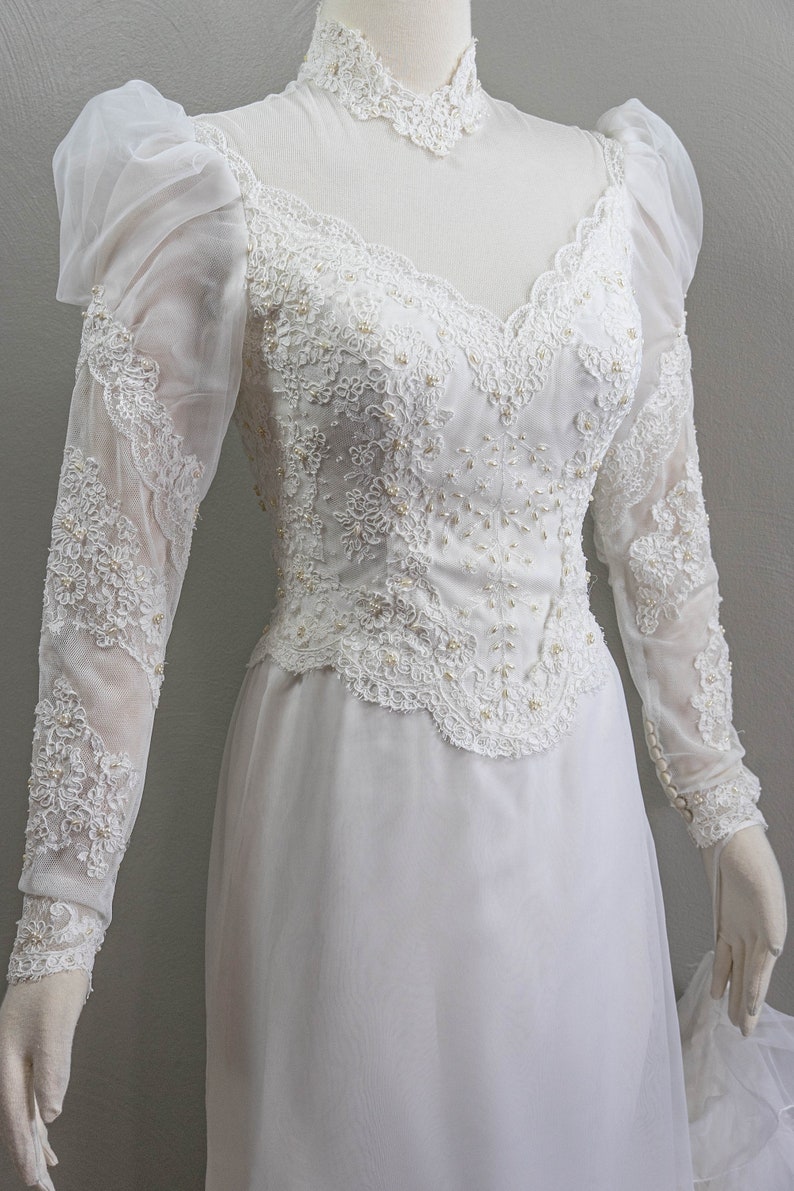 May include: A white wedding dress with long sleeves and a high neckline. The dress is made of lace and features a fitted bodice and a flowing skirt.