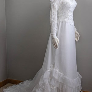 May include: A white wedding dress with long sleeves and a lace bodice. The skirt has multiple layers of tulle and lace trim.