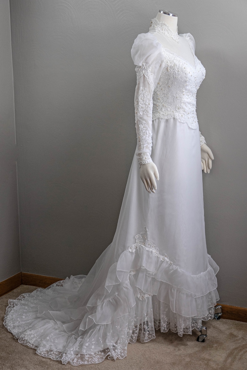 May include: A white wedding dress with long sleeves and a lace bodice. The skirt has multiple layers of tulle and lace trim.