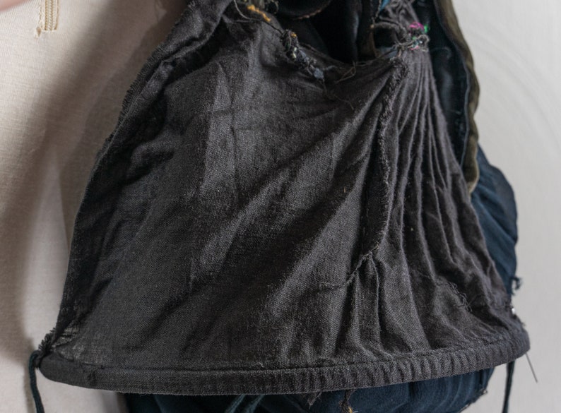 May include: A black hooded garment with a drawstring closure. The hood is made of a soft, textured fabric and has a gathered look. The garment is worn over a blue denim jacket.
