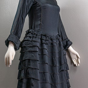 May include: A black dress with a ruffled skirt and sheer sleeves. The dress has a lace neckline and is fitted through the bodice.