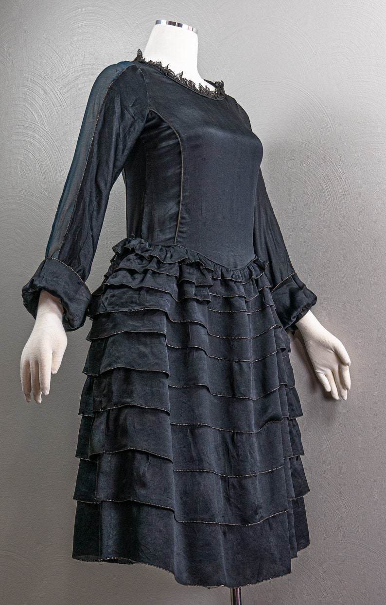 May include: A black dress with a ruffled skirt and sheer sleeves. The dress has a lace neckline and is fitted through the bodice.