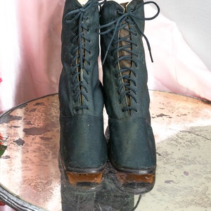 May include: A pair of black lace-up boots with brown soles. The boots are sitting on a round, mirrored surface.