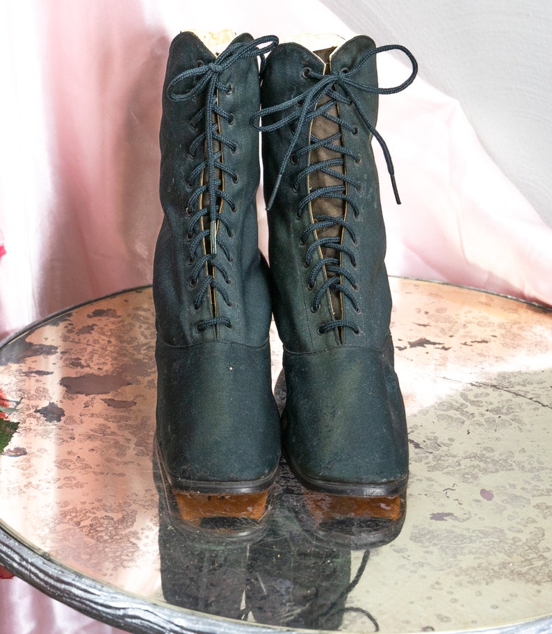May include: A pair of black lace-up boots with brown soles. The boots are sitting on a round, mirrored surface.