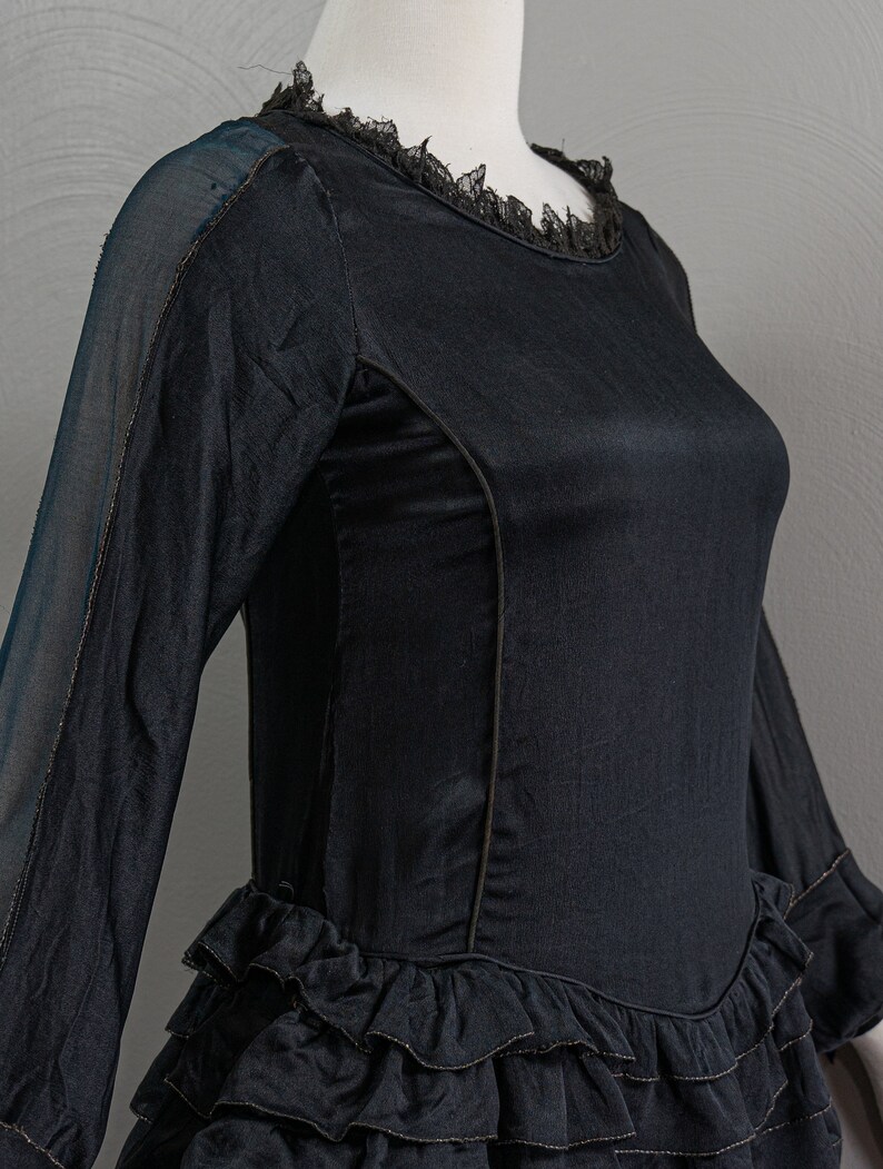 May include: A black dress with a lace neckline and a tiered ruffle skirt. The dress has long sleeves and a fitted bodice.