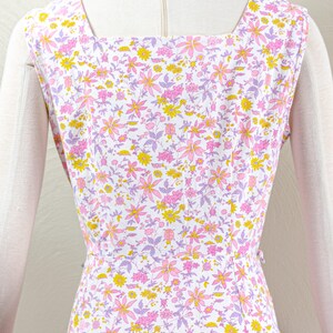 Puede incluir: Vestido sin mangas con cuello cuadrado, con un estampado floral de flores rosas, amarillas y moradas sobre fondo blanco. El vestido est&aacute; entallado en la cintura y tiene cierre de botones en la espalda.