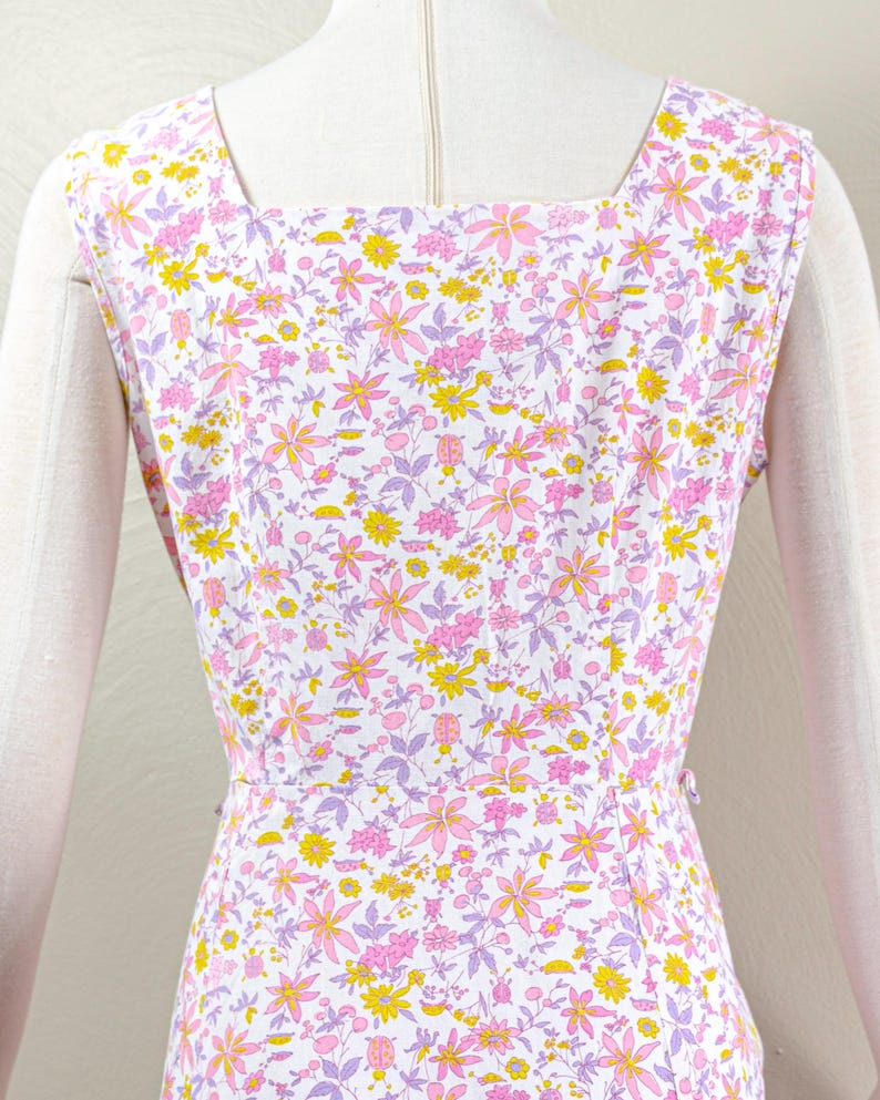 Puede incluir: Vestido sin mangas con cuello cuadrado, con un estampado floral de flores rosas, amarillas y moradas sobre fondo blanco. El vestido est&aacute; entallado en la cintura y tiene cierre de botones en la espalda.