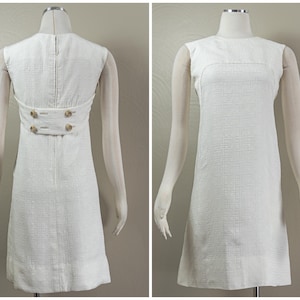 Puede incluir: Un vestido blanco sin mangas de tejido texturizado con dos botones dorados en la espalda.