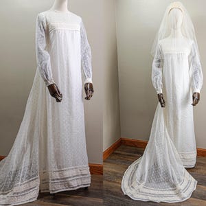 May include: A white vintage wedding dress with a lace trim and a dotted pattern. The dress has long sleeves and a flowing skirt. The dress is being displayed on a mannequin.