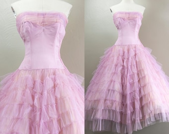 May include: A strapless pink tulle dress with multiple layers of ruffles. The bodice is a solid pink satin.