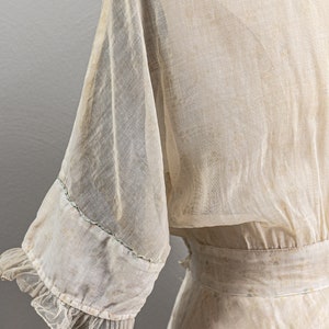 May include: A sheer white dress with a ruffled trim on the sleeves. The dress has a fitted bodice and a flowing skirt. The fabric is delicate and has a vintage feel.