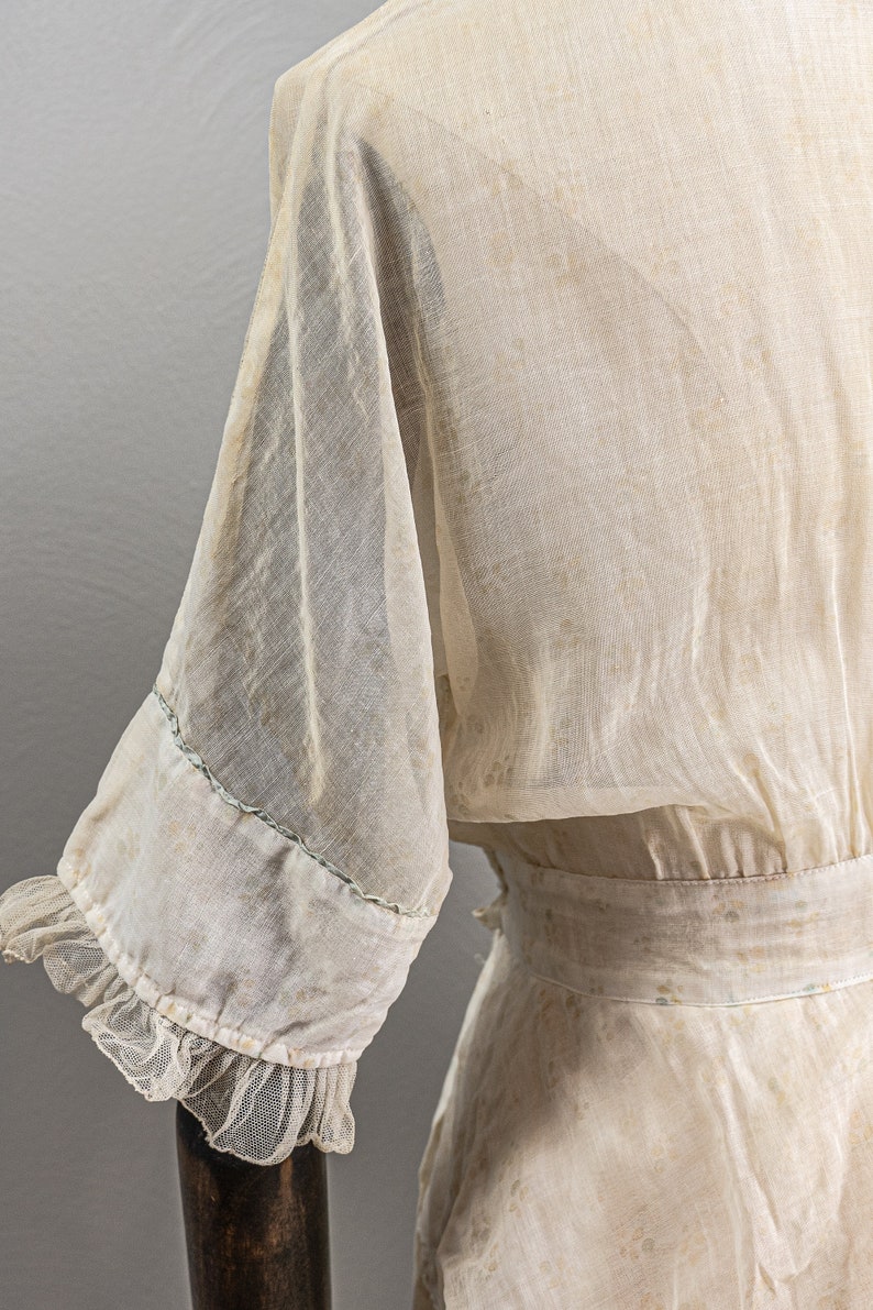 May include: A sheer white dress with a ruffled trim on the sleeves. The dress has a fitted bodice and a flowing skirt. The fabric is delicate and has a vintage feel.