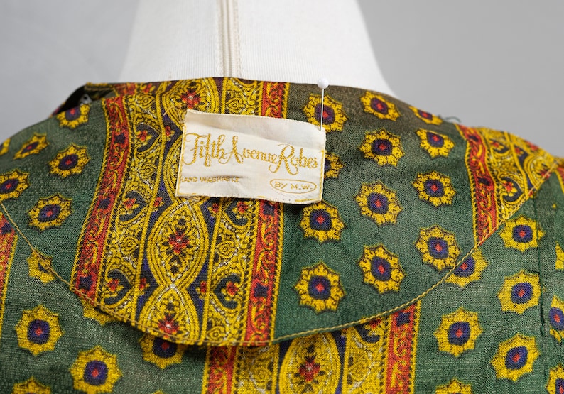 May include: A green and yellow patterned fabric with a white label that reads "Fifth Avenue Robes, Hand Washable, By M.W."