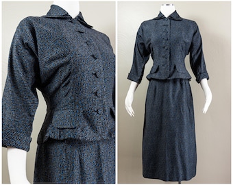 May include: A vintage two-piece suit in a textured navy blue fabric with flecks of blue and brown. The jacket has a notched collar, three-quarter sleeves, and decorative buttons. The skirt is a knee-length pencil skirt.