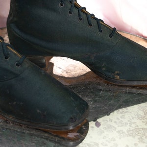 May include: A pair of black satin ankle boots with lace-up closures. The boots have a low heel and are slightly worn.