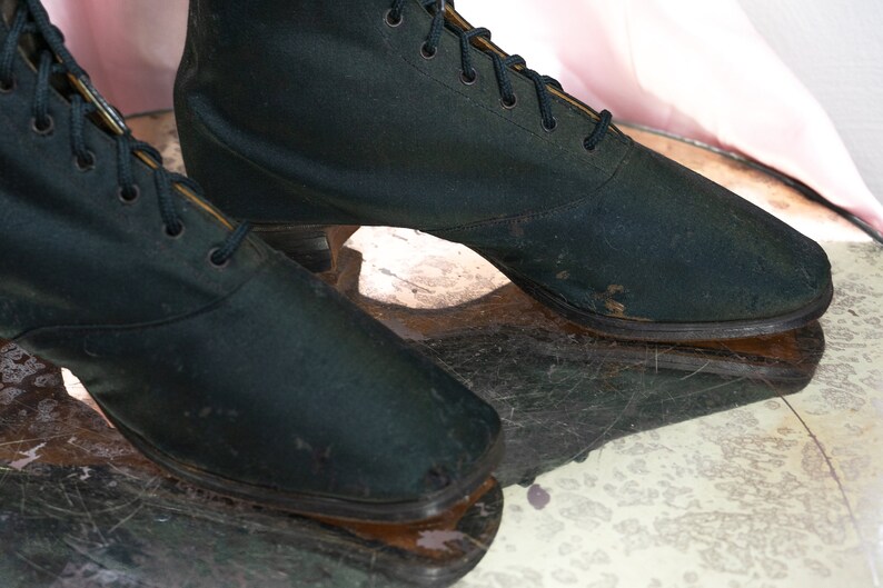 May include: A pair of black satin ankle boots with lace-up closures. The boots have a low heel and are slightly worn.