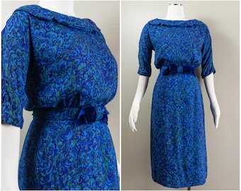 May include: A blue and green patterned dress with a velvet belt. The dress has a short sleeve and a round neckline.