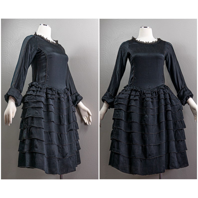 May include: A black satin dress with a ruffled skirt and long sleeves. The dress has a lace trim at the neckline.