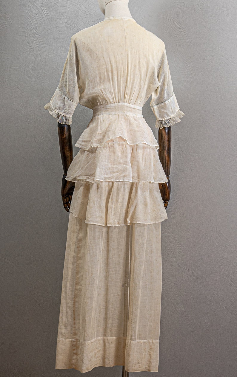 May include: A white cotton dress with a tiered skirt and a fitted bodice. The dress has a V-neckline and short sleeves with ruffles.