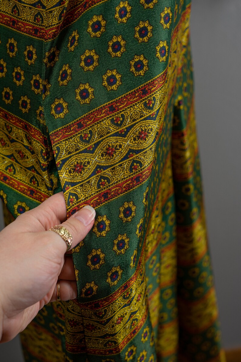 May include: Green fabric with a repeating pattern of yellow and blue flowers and a red, yellow, and blue paisley border.
