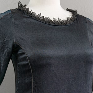 May include: A black long-sleeved dress with a lace trim around the neckline. The dress has a fitted bodice and a flowing skirt.