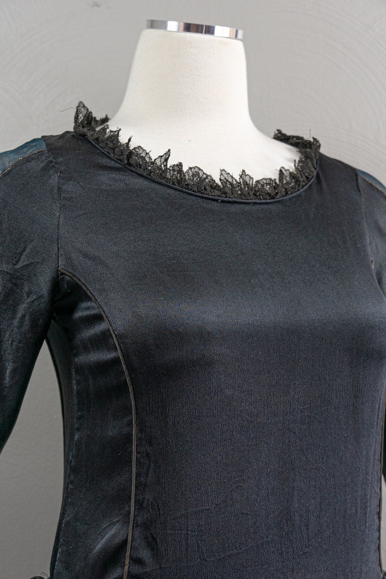 May include: A black long-sleeved dress with a lace trim around the neckline. The dress has a fitted bodice and a flowing skirt.