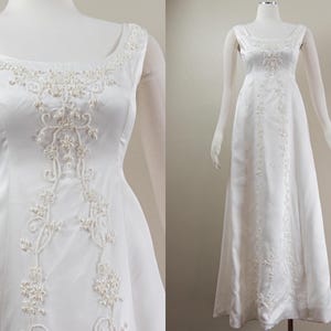 Puede incluir: Un vestido de novia blanco sin mangas con escote redondo y un patrón floral de cuentas. El vestido tiene un corpiño ajustado y una falda fluida.