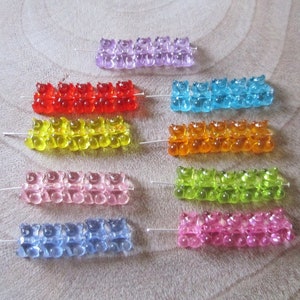 Könnte beinhalten: Zehn Reihen von Gummibärchen-Perlen in verschiedenen Farben, darunter Lila, Rot, Gelb, Rosa, Blau, Grün und Orange. Die Perlen sind auf dünnen Drähten aufgefädelt.