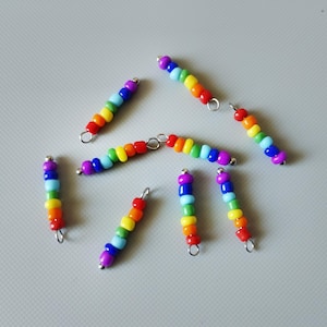 Könnte beinhalten: Acht regenbogenfarbene Perlenstränge mit silbernen Sprungringen an jedem Ende. Jeder Strang hat eine andere Farb Reihenfolge des Regenbogens.