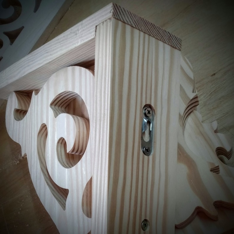 Op de afbeelding: Een houten plankensteun met een decoratief, sierlijk ontwerp. De steun is gemaakt van licht hout en heeft een metalen beugel aan de zijkant.