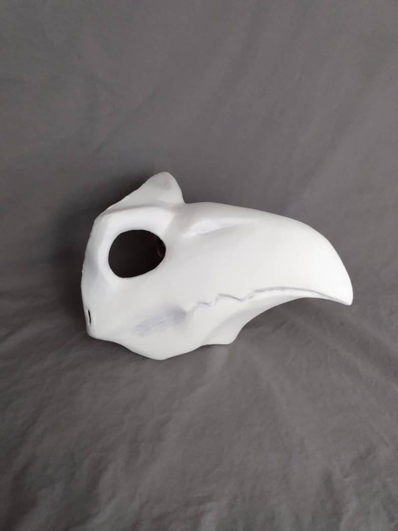 May include: A white, unpainted, plastic mask with a long, curved beak. The mask has a single eye hole and a small hole on the side.