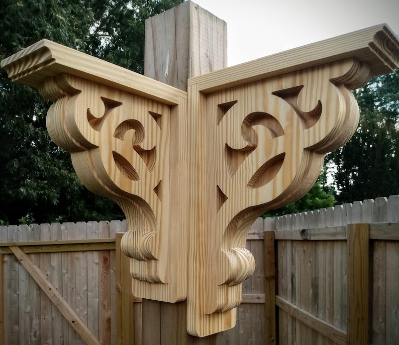 Op de afbeelding: Twee houten consoles met ingewikkelde uitsnijdingen en een decoratief ontwerp. De consoles zijn bevestigd aan een houten paal en zijn afgewerkt in een natuurlijke houtkleur.