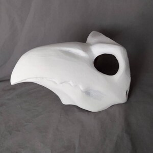 May include: White plaster mask with a long, curved beak and a single eye hole. The mask is designed to cover the entire face.