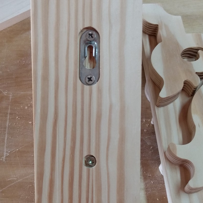 Op de afbeelding: Close-up van een houten plank met een metalen haak en twee schroeven. De plank is gemaakt van licht hout met een natuurlijke nerf.
