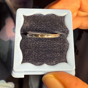 May include: A silver ring with a simple design sits in a blue velvet ring box.