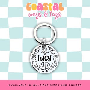 May include: Silver dog tag with a seashell design and the name "Lucy" engraved on it. The tag is attached to a silver key ring.