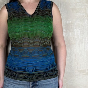 Op de afbeelding: Een mouwloos, gestreept shirt met een v-hals. Het shirt is een gradiënt van groen, blauw en zwart.