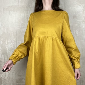 May include: A mustard yellow mini dress with long sleeves and a gathered waist. The sleeves have elastic cuffs.