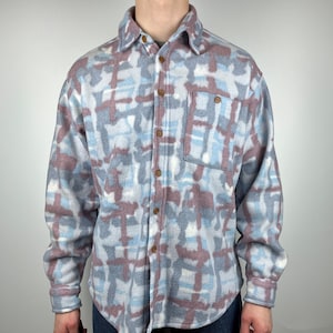 May include: A long-sleeved button-up shirt with a blue, white, and pink abstract pattern. The shirt has a button-down collar and a chest pocket.