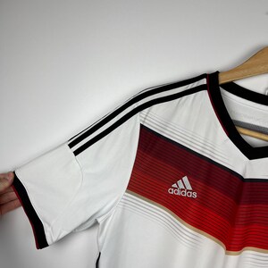 May include: White soccer jersey with black and red stripes, featuring the Adidas logo and the word "adidas" in white lettering.
