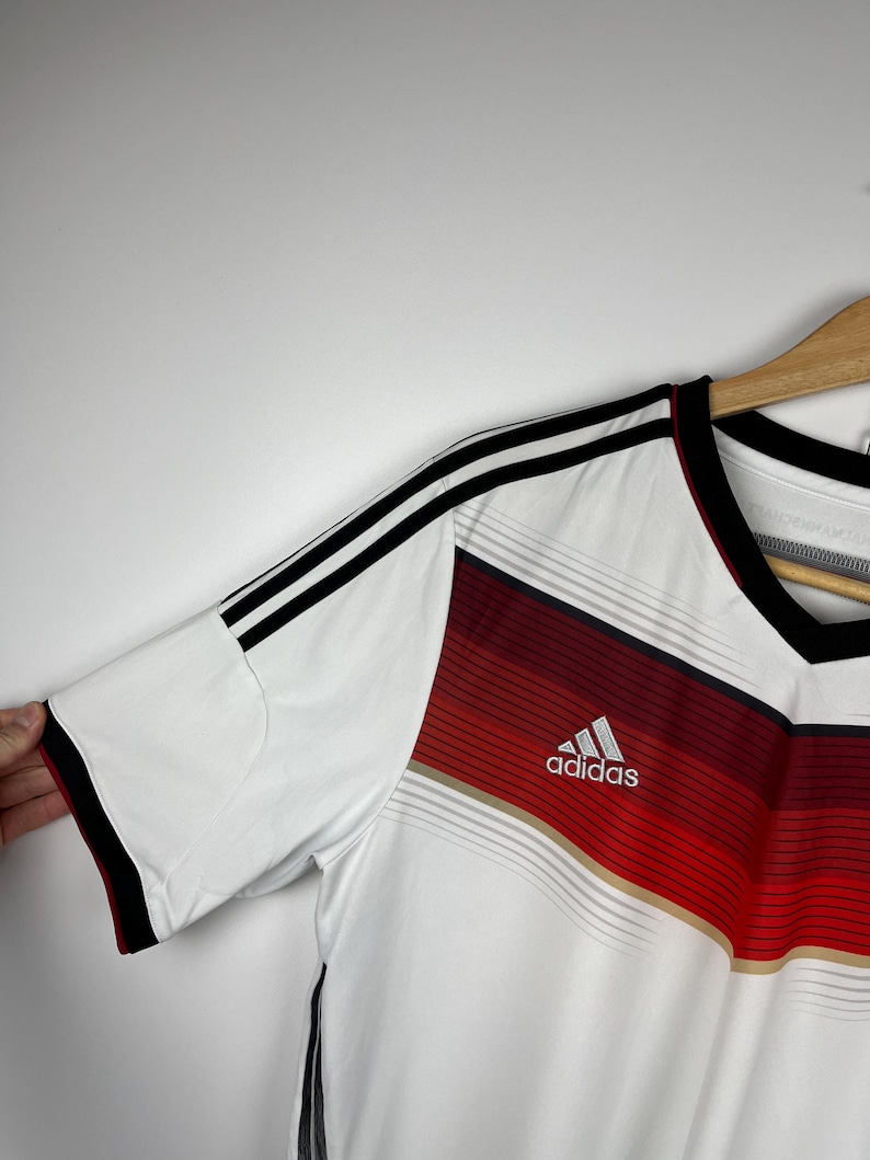 May include: White soccer jersey with black and red stripes, featuring the Adidas logo and the word "adidas" in white lettering.