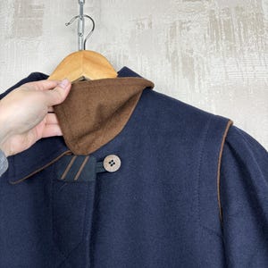 May include: A navy blue wool coat with brown leather trim and a brown corduroy collar. The coat has a single button closure and a brown button on the collar.