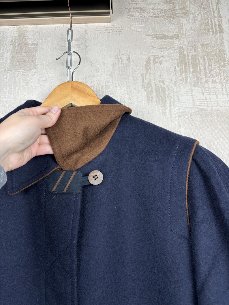 May include: A navy blue wool coat with brown leather trim and a brown corduroy collar. The coat has a single button closure and a brown button on the collar.