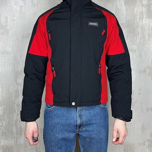 May include: Black and red Ferrari jacket with a high collar and zippered pockets. The jacket has a black body with red shoulder and sleeve accents. The Ferrari logo is visible on the chest.