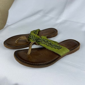 May include: A pair of brown leather sandals with green suede straps and metal chain detailing.