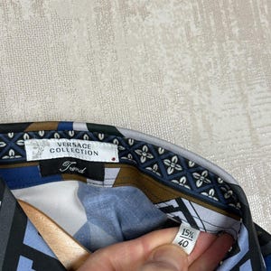 May include: Versace Collection shirt with a geometric pattern in blue, black, and brown. The collar features a floral design. The label reads "Versace Collection Trend" and size 15 1/2, 40.